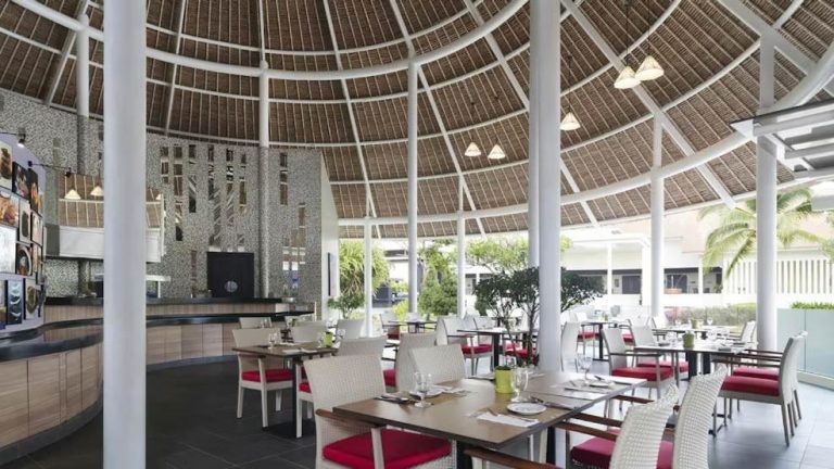 Restaurante tropical con techo de paja y mesas con cojines rojos en Golden Palm Tree Suite Sepang Malaysia