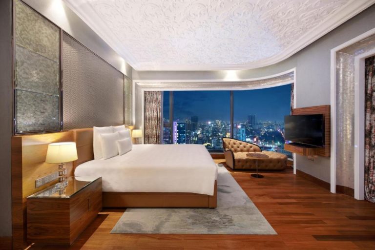 Suite de lujo con cama king y vistas panorámicas nocturnas de la ciudad en The Reverie Saigon