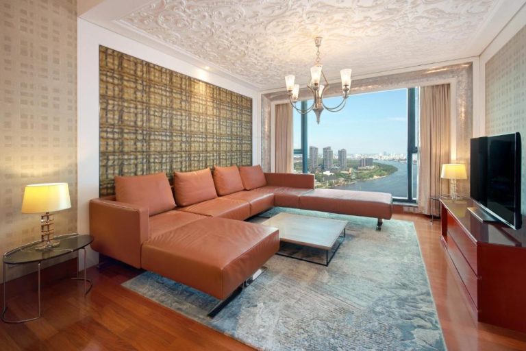 Lujoso salón con sofá de cuero y vistas panorámicas al río en The Reverie Saigon Residential Suites