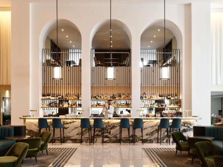 Elegante bar con barra de mármol y estantes de licores bajo arcos blancos en el Swissotel Sydney