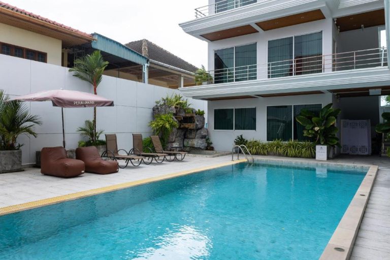 Piscina exterior con tumbonas y sombrilla del Peranakan House rodeada de jardín tropical
