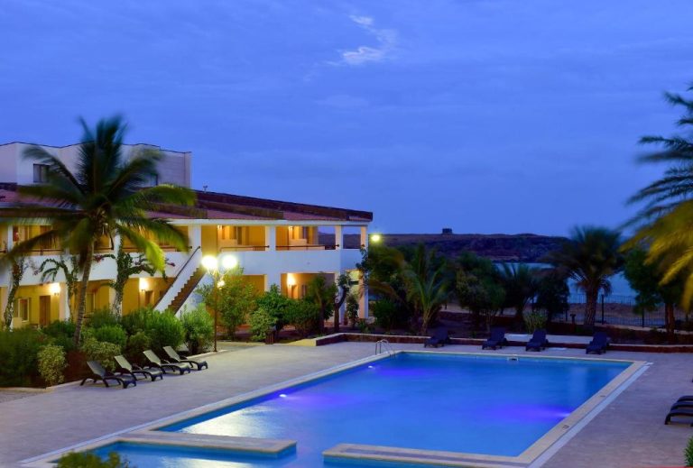 Piscina exterior iluminada de noche con tumbonas y palmeras en el Pestana Trópico
