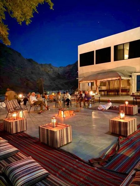 Terraza exterior nocturna con linternas y cojines árabes del Wadi Al Arbeieen Resort entre montañas