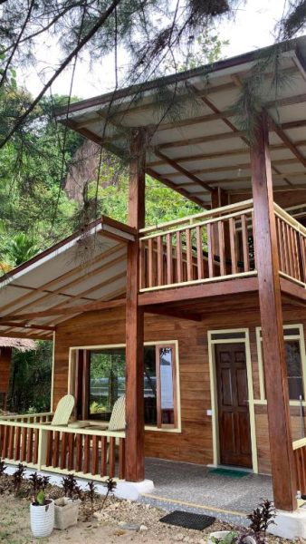 Cabaña de madera de dos pisos con terraza y balcón en Ricky's Beach House rodeada de naturaleza