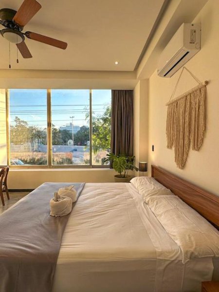 Habitación doble con cama king size, ventilador de techo y ventanal con vista exterior en Balam Suites