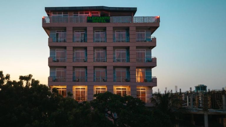 Fachada exterior del Elephanto Hotel LTD al atardecer con balcones y letrero iluminado en verde