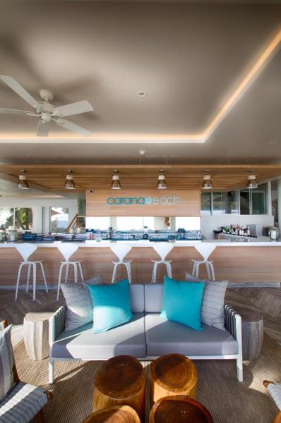 Bar y zona lounge interior del hotel CaranaBeach con sofás grises y cojines turquesa