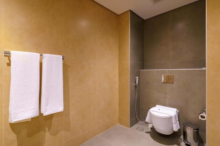 Baño moderno con inodoro suspendido y toallas blancas en Jarzez Inn Hotel Azaiba