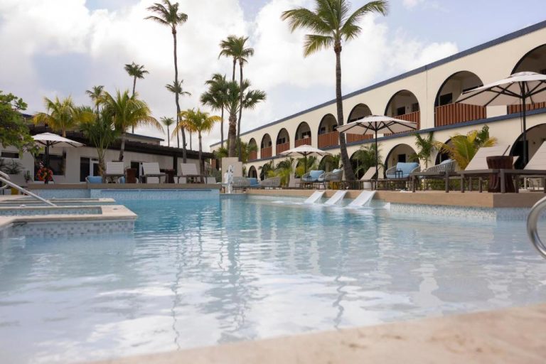 Piscina exterior con tumbonas y palmeras del voco Surfside Aruba by IHG con vistas al edificio