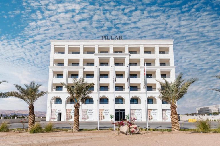 Fachada exterior del Golden Pillar Hotel con palmeras y arquitectura blanca bajo cielo azul