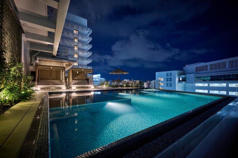 Piscina exterior iluminada de noche en The Royal Park Hotel Iconic Naha con vistas a la ciudad