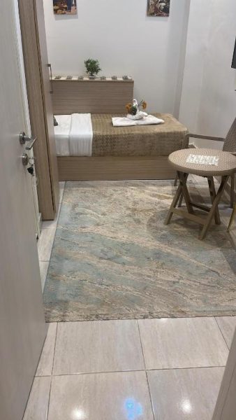 Habitación individual del Crown Home con cama, alfombra decorativa y mesa auxiliar de madera