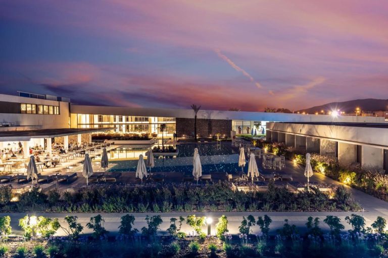 Piscina exterior iluminada al atardecer con tumbonas y sombrillas del Gennadi Grand Resort en Rodas
