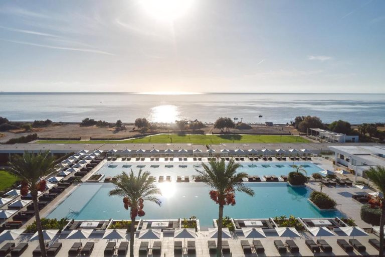Piscina exterior con tumbonas y palmeras frente al mar en Gennadi Grand Resort Premium All Inclusive