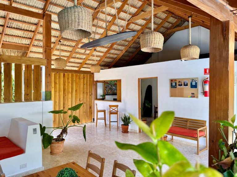 Área de recepción y lobby con techo de palma y tablas de surf en La Curadiña Encuentro Surf Hotel