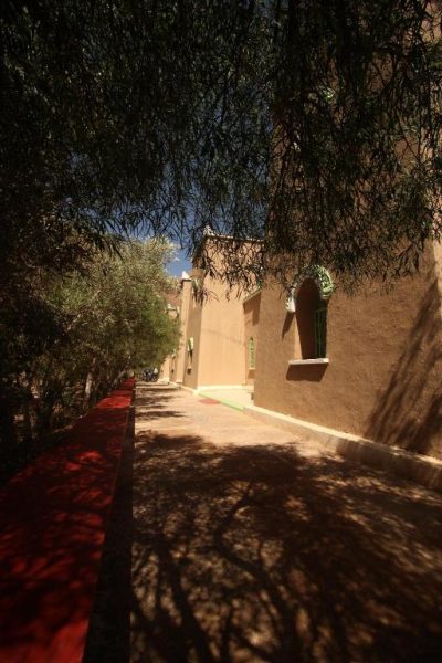 Pasillo exterior con palmeras y alfombra roja del Kasbah Hotel Camping Jurassique en Marruecos