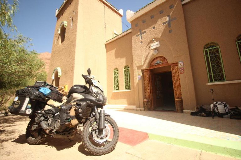 Fachada principal del Kasbah Hotel Camping Jurassique con motocicleta de aventura aparcada en el exterior
