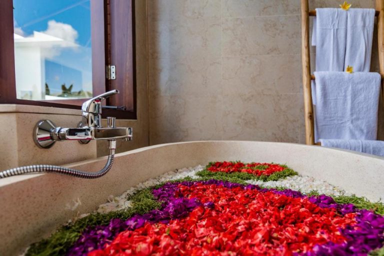 Bañera de piedra decorada con pétalos de flores tropicales en Svadarma Bali Villa by Dhananjaya