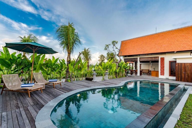 Piscina privada con terraza de madera y tumbonas en Svadarma Bali Villa rodeada de vegetación tropical