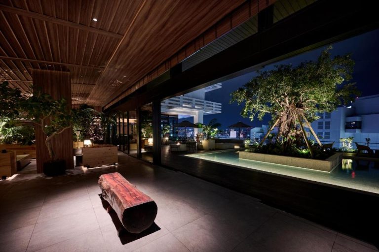 Terraza con piscina iluminada y jardín tropical de noche en The Royal Park Hotel Iconic Naha