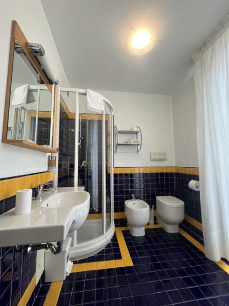 Baño completo con ducha, bidé y lavabo con azulejos negros y amarillos en Hotel Liberty