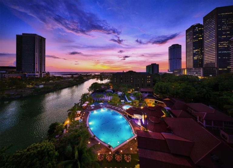 Piscina exterior iluminada del Hilton Colombo con vistas al río y skyline de la ciudad al atardecer