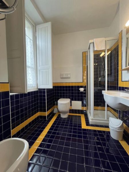 Baño con azulejos azules y amarillos, ducha y bidé del Hotel Liberty