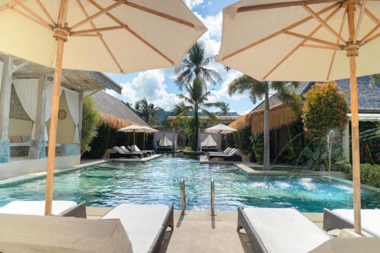 Piscina exterior con tumbonas y sombrillas del Rascals Hotel Adults Only rodeada de palmeras tropicales
