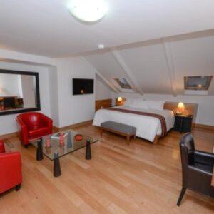 Suite junior con cama doble, sillones rojos y suelo de madera en Hotel Plaza de Armas Cusco