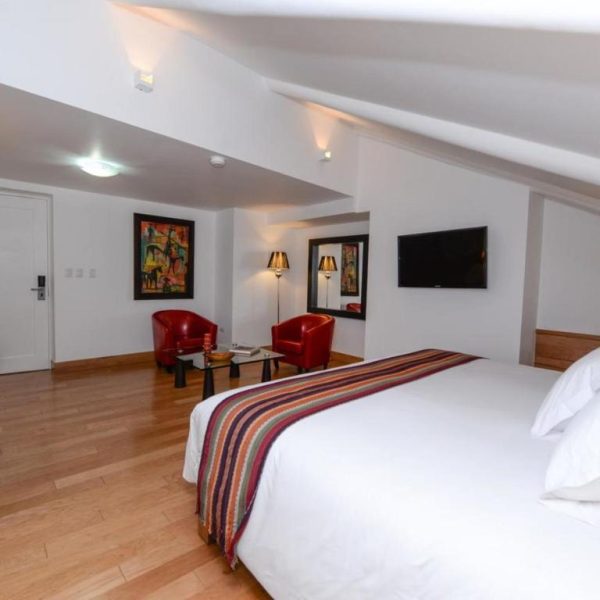 Suite con cama doble, suelo de madera y sillones rojos en Hotel Plaza de Armas Cusco