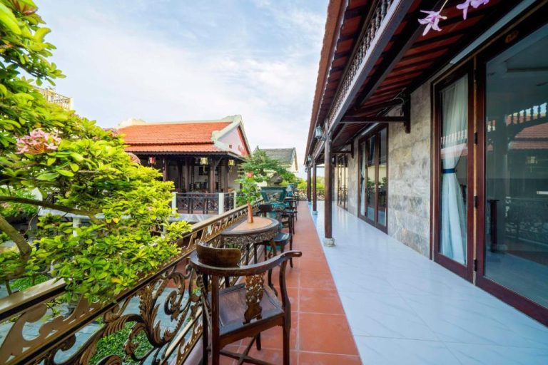 Terraza colonial con sillas de madera tallada y jardín tropical en Bonsai Villa Hoi An