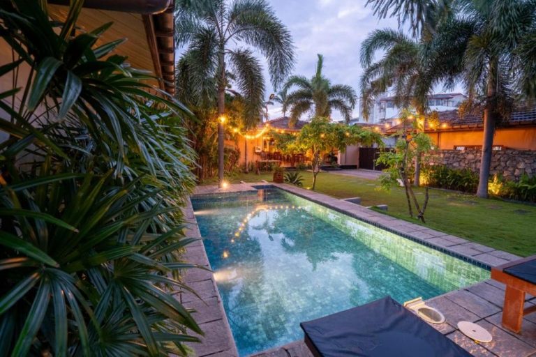 Piscina exterior con jardín tropical e iluminación nocturna en The Barns Villas and Restaurant