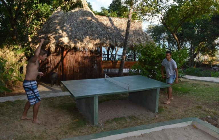 Dos jóvenes jugando ping pong al aire libre en Laguna Beach Club con cabaña de paja al fondo