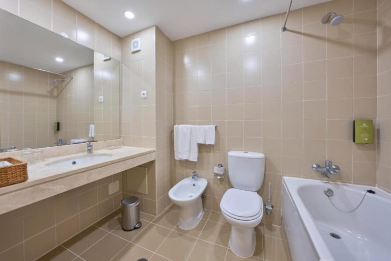 Baño completo con bañera, bidé y lavabo del Caloura Hotel Resort en azulejos beige
