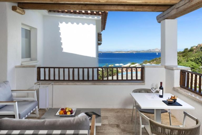 Terraza con mesa de vino y sofás con vistas al mar azul en Hotel La Bisaccia Cerdeña
