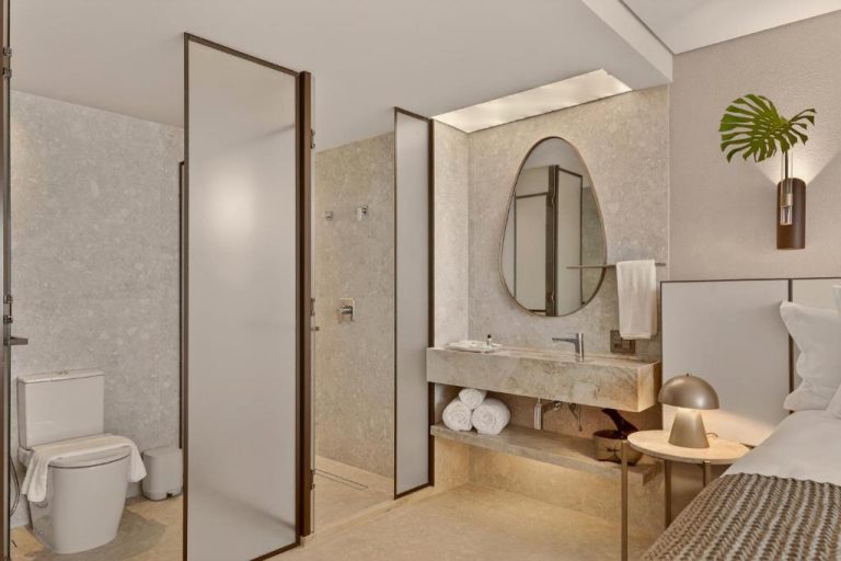 Baño de lujo con lavabo de mármol, ducha y espejo oval en Venti Hotel by Brisa Hotéis