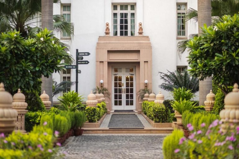 Entrada principal del hotel The Imperial New Delhi con jardines tropicales y arquitectura colonial clásica