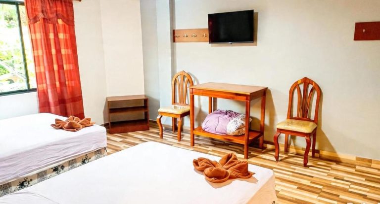 Habitación triple del Hotel Girasol con dos camas, escritorio de madera, sillas y televisión en la pared