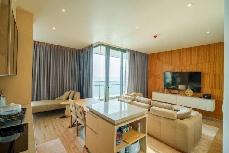 Salón moderno con sofás beige, cocina americana y vistas al mar en Luxury 2BR Sea View Apartment