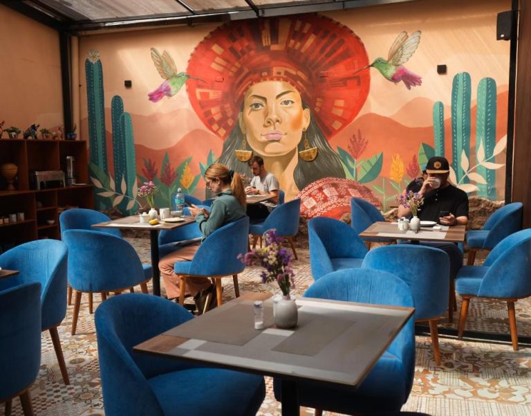 Restaurante del Way Kap Hostel Cusco con mural indígena, sillas azules y ambiente andino colorido