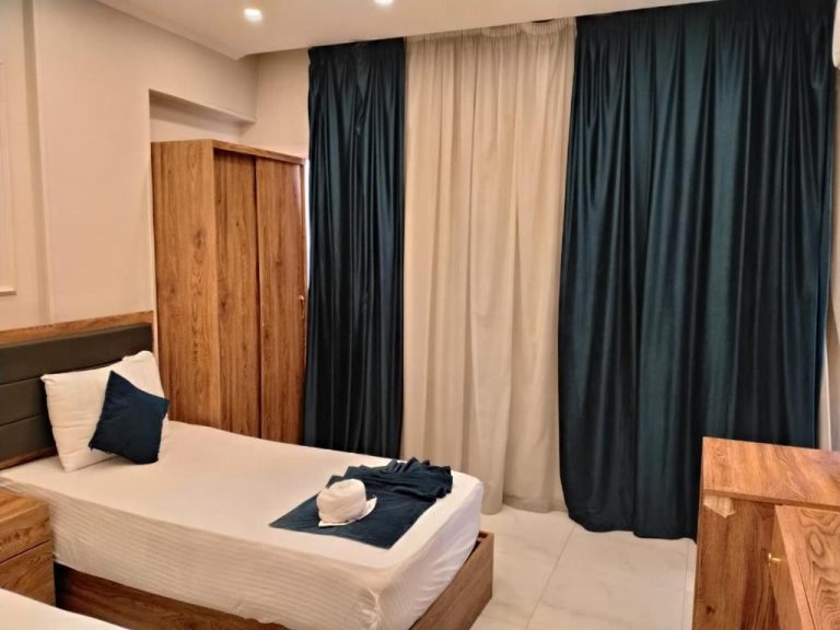 Habitación doble con cama, armario de madera y cortinas azules en Up Town Crown Hotel