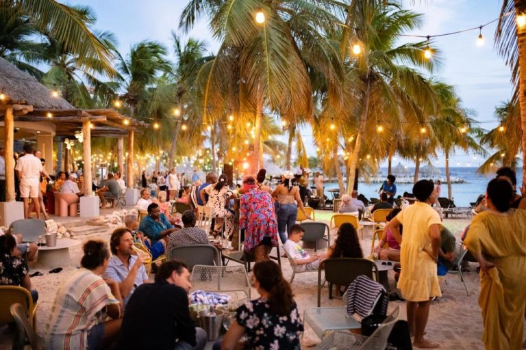 Terraza beach bar con ambiente nocturno y palmeras en The Ivy Blue Bay Curaçao Golf & Beach Resort