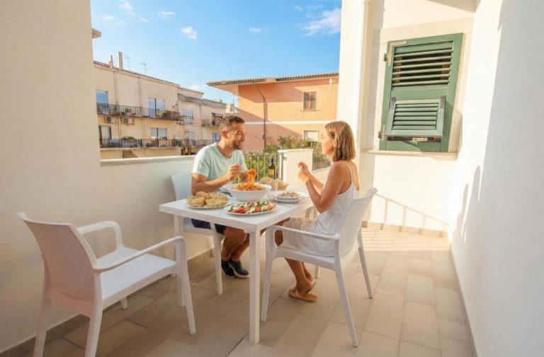 Pareja disfrutando de una comida en la terraza exterior de Sea Wind Apartments & Suites con vistas al pueblo