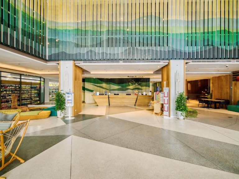 Amplio lobby y recepción del hotel ibis Styles Nha Trang con mural decorativo de montañas verdes