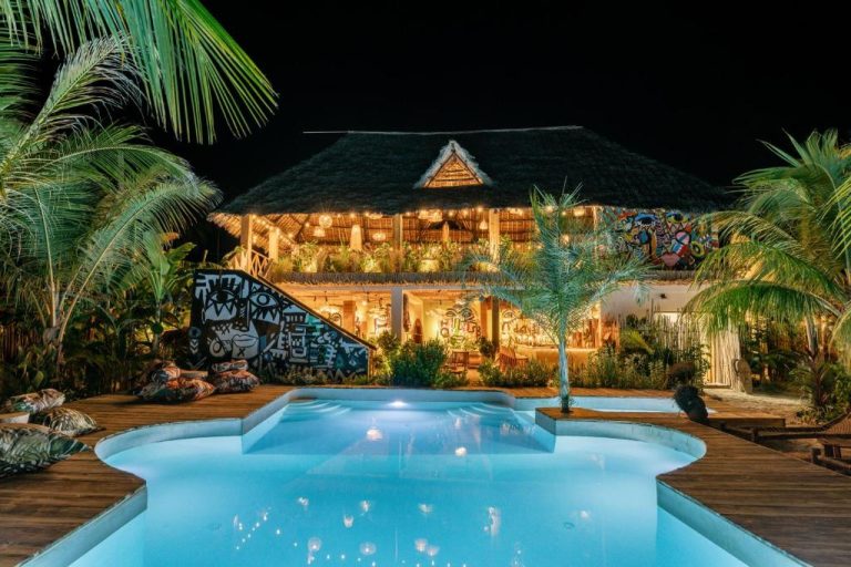 Piscina exterior iluminada de noche en el Oke Ani Boutique Hotel con arte mural y techo de palapa