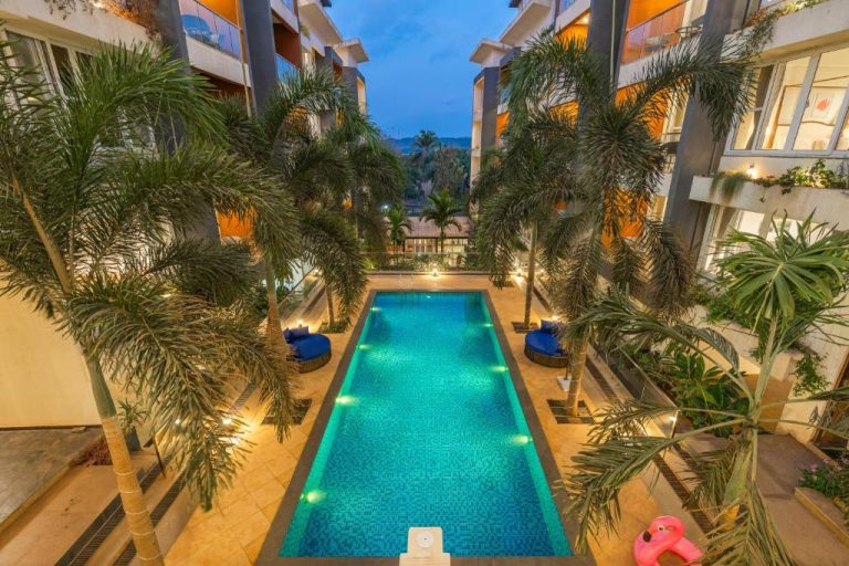 Piscina iluminada con palmeras tropicales en Perfectstayz Premium Carnival Suites cerca de Candolim, Goa