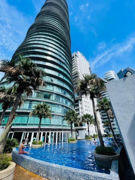 Piscina infinita exterior con palmeras y torre helicoidal del Vortex KLCC Apartment en Kuala Lumpur