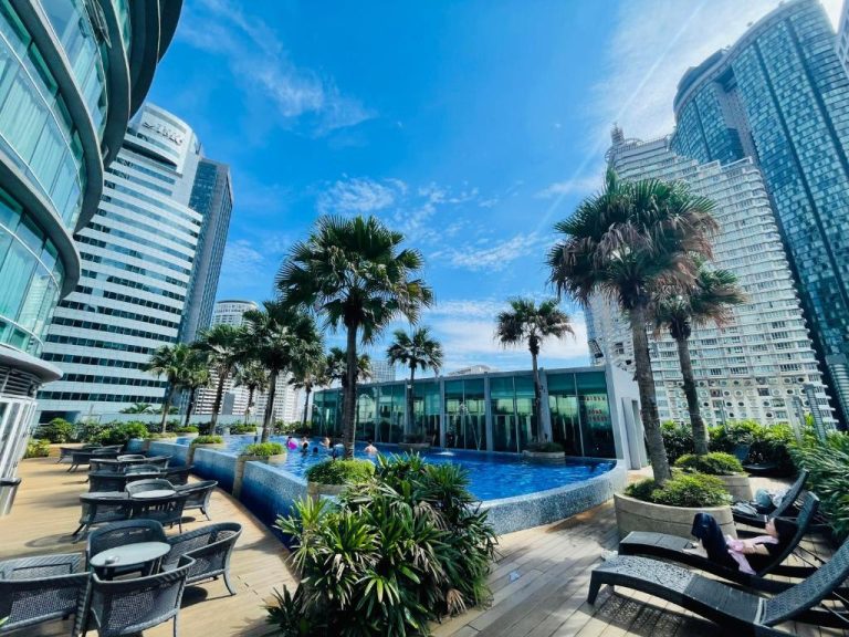 Piscina exterior con palmeras y tumbonas del Vortex KLCC Apartment rodeada de rascacielos en Kuala Lumpur