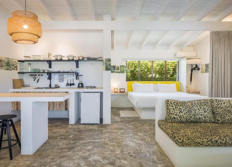 Estudio con cocina equipada, sofá leopardo y cama doble con cabecero amarillo en El Encuentro Surf Lodge