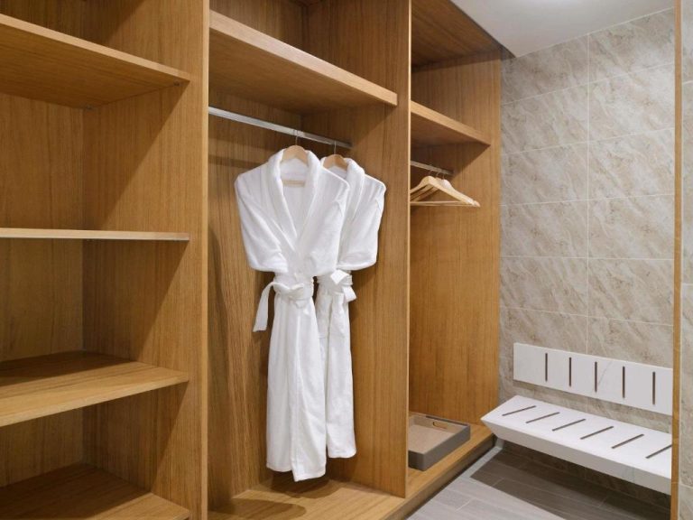 Vestidor de madera con albornoces blancos y zona de ducha en Mövenpick Hotel Ghala Muscat